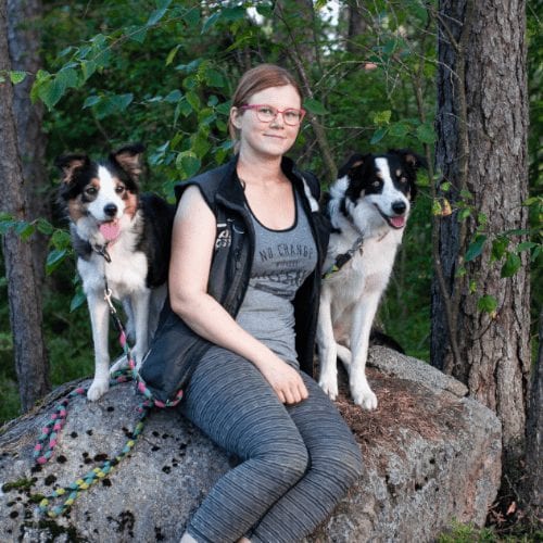 Janita Riikonen istuu metsässä kivellä kahden koiransa kanssa.